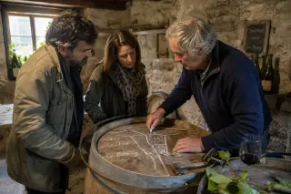 Two winemakers reading notes together near oak barrels in a stone-walled Rioja cellar, with soft daylight and a natural, authentic atmosphere.